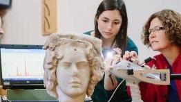 赌博娱乐平台网址大全 professor 和 her student examine an ancient sculpted bust.